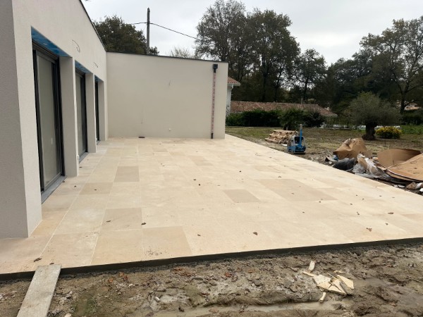 Terrasse extérieure réalisée en dalles de pierre naturelle beige, chantier d’aménagement extérieur par JÉROME TP.