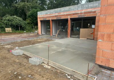 Coulage d’une dalle béton pour terrasse extérieure sur chantier de construction - JÉROME TP Réalisation d’une dalle béton fraîchement coulée devant une maison en construction, travaux de terrassement et gros œuvre par JÉROME TP.