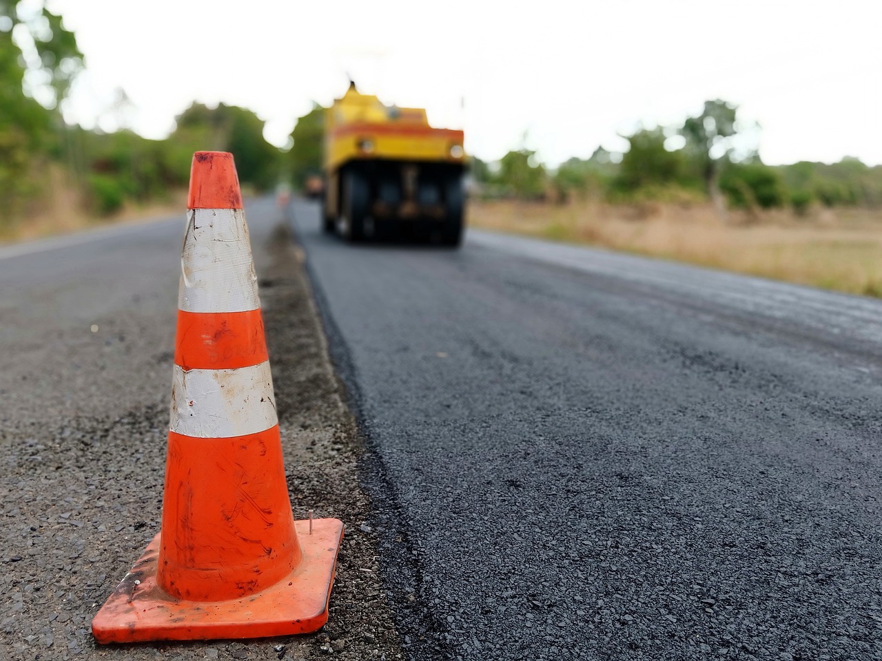 Réfection de chaussée en cours avec pose d’enrobé, cône de signalisation en premier plan pour balisage du chantier.